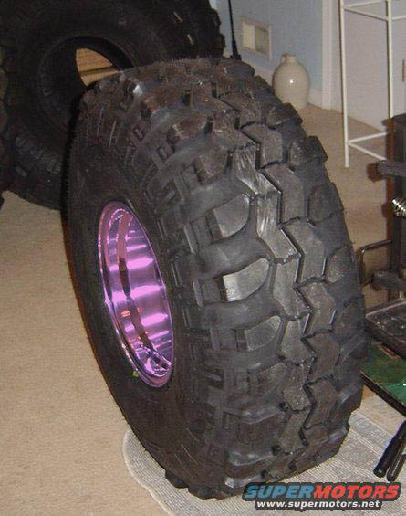 1989 Ford Bronco - A single off-road tire with an aggressive tread pattern and a vibrant purple wheel is the focus of the image.