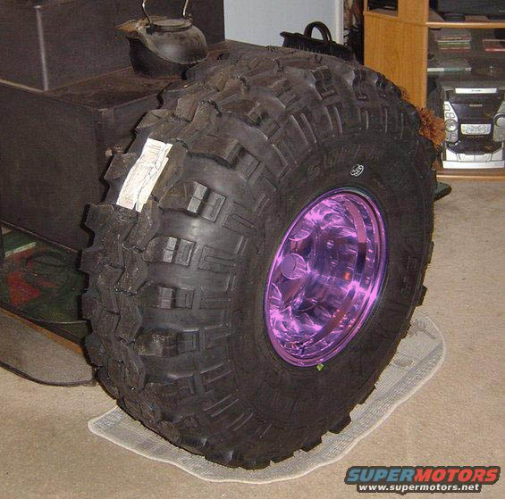 Oversized off-road tire with purple-tinted rim, mounted on an unseen vehicle