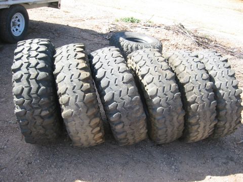 1966 Ford Bronco - A collection of aggressive tread off-road tires are displayed outdoors, with a trailer wheel in the background.