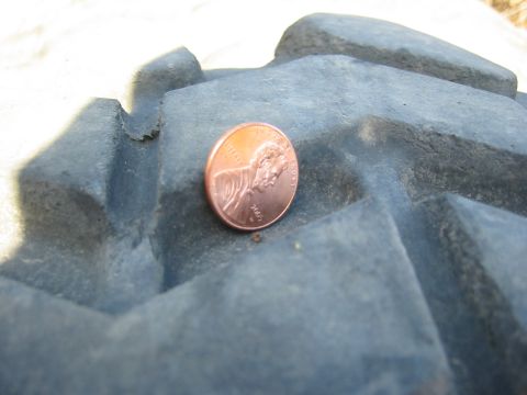 1966 Ford Bronco - A close-up of a tire tread shows its aggressive pattern, with a penny placed on it for size comparison.