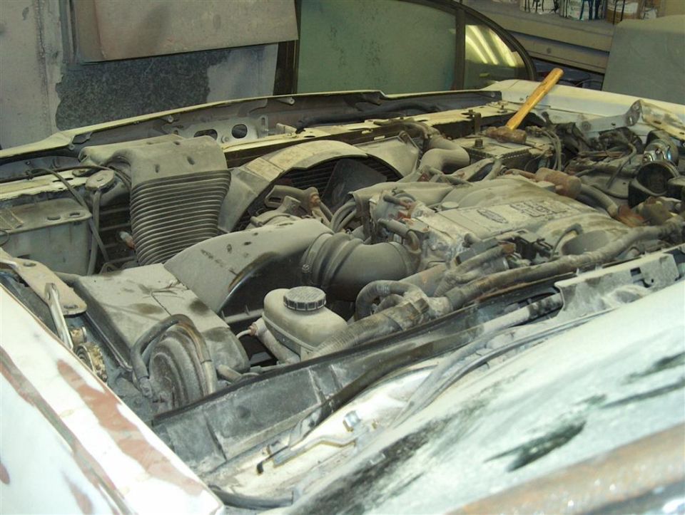 Dusty engine bay of a vehicle with hood open in a workshop