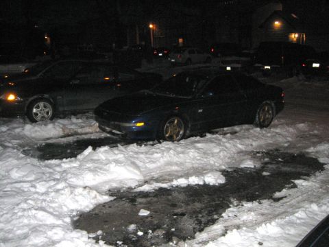 1995 Ford Probe - Two cars are parked in a snowy lot at night, with one car partially obscured by snowdrifts.