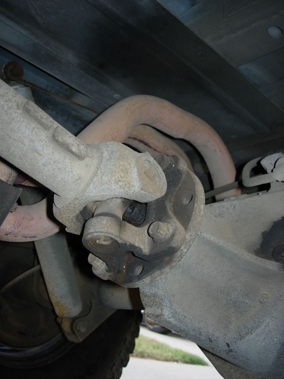 Close-up of driveshaft U-joint and exhaust pipes underneath a vehicle
