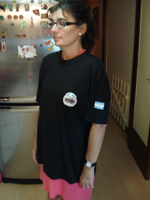 1986 Ford Bronco - A woman stands in front of a refrigerator covered in magnets, wearing a black t-shirt with an Argentinian flag patch on the sleeve.