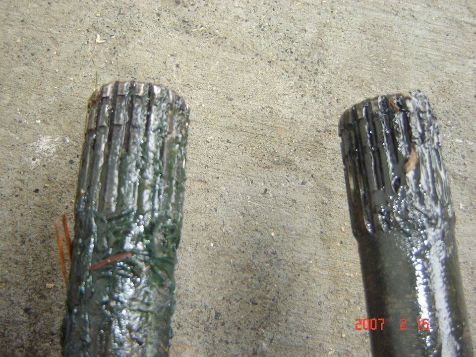 Two greasy drive shafts with splined ends resting on a concrete surface