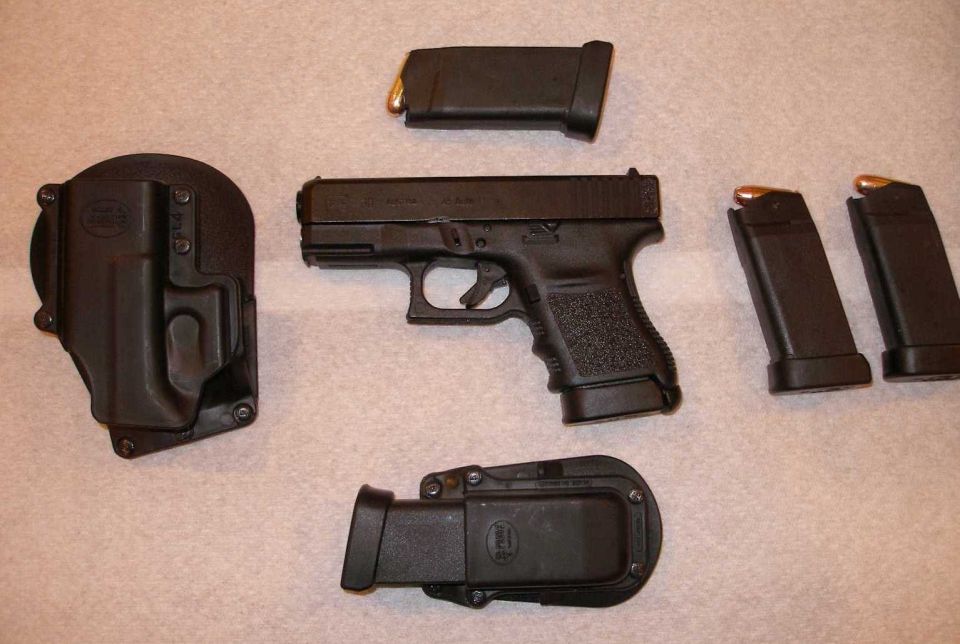 Black pistol with holster, mag pouch, and three magazines on carpet