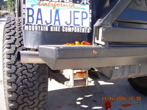 1990 Ford Bronco - Close-up of a dark vehicle's rear tubular bumper and exhaust tip with a Baja Jep mountain bike components license plate frame.