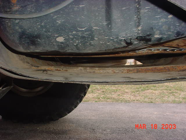Underside view of a rusty tank mounting flange and gap above a knobby off-road tire