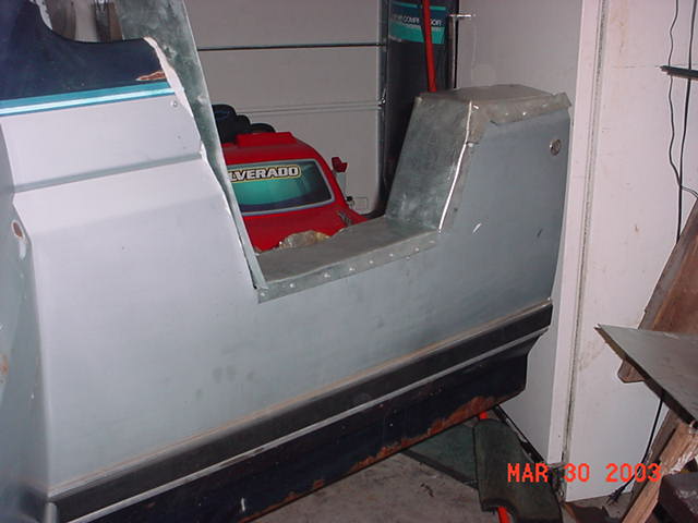 Primer-gray fiberglass truck body panel in garage with red Silverado lawn mower behind