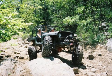 1991 Ford F-150 - A modified Jeep navigates a rocky, off-road trail with two occupants.