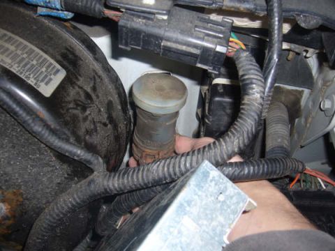 1996 Mercury Grand Marquis - Brake fluid reservoir and master cylinder assembly with visible wiring and a hand reaching into the engine bay.
