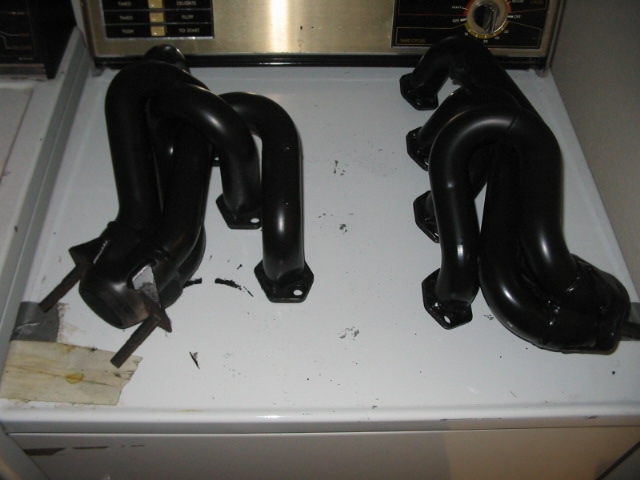 two black exhaust headers sitting on a white surface