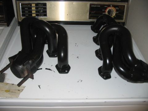 1991 Ford Bronco - Two black exhaust headers are displayed on a white surface, with a washing machine's control panel visible in the background.