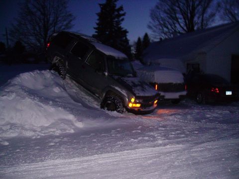 2000 Chevrolet Tahoe - A dark SUV is stuck in a snowdrift on a winter night, with two other vehicles parked nearby.
