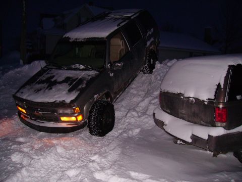 2000 Chevrolet Tahoe - Two SUVs are partially buried in snow, indicating difficult driving conditions.