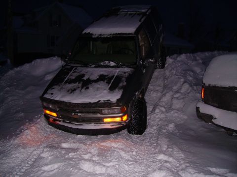 2000 Chevrolet Tahoe - A dark 2000 Chevrolet Tahoe is partially buried in snow, with another vehicle visible to the right.
