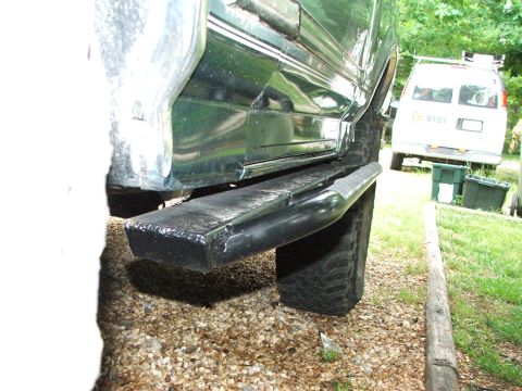 1996 Ford Bronco - The side of a green SUV is shown with a black running board and large tire. A white van is visible in the background.