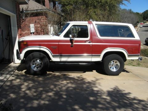 1986 Ford Bronco - This two-tone red and white Ford Bronco is seen from the side, parked in a driveway.