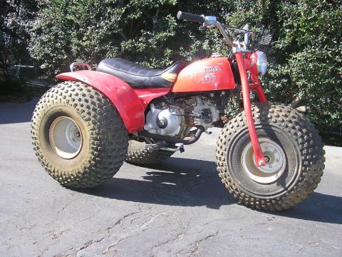 1900 Honda Big Red - A red Honda ATC 110 three-wheeler is shown from a 3/4 front angle, parked outdoors.