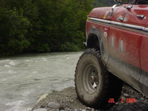 1978 Ford Bronco - A red 1978 Ford Bronco is parked by a flowing river, showing its off-road tires and weathered exterior.