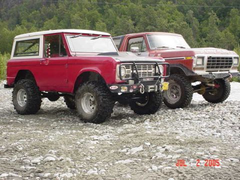 1978 Ford Bronco - Two Ford Broncos are parked on a gravelly surface with trees in the background.