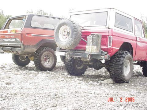 1978 Ford Bronco - Two Ford Broncos, a red 1978 model and a red and black model, are parked on a rocky terrain.