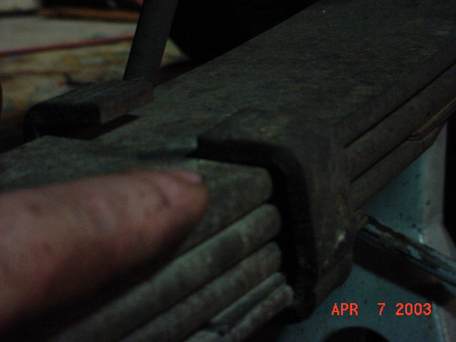 Close-up of a rusty leaf spring pack and retaining clip in a vise, dated April 2003