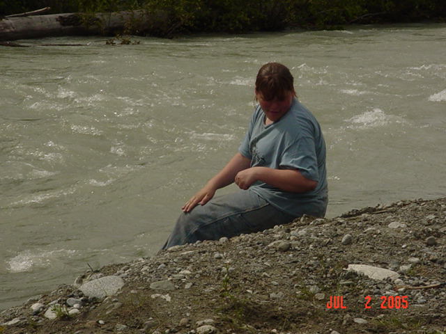 person sitting by a fast-moving river on a rocky shore, date stamp shows JUL 2 2005