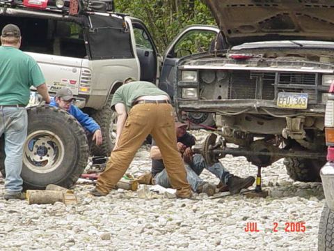 1978 Ford Bronco - Several people are gathered around off-road vehicles, appearing to perform maintenance on one of them.