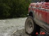 1978 Ford Bronco - A red off-road vehicle navigates through a shallow body of water, its large tires kicking up spray.