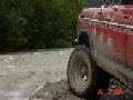 1978 Ford Bronco - A red 1978 Ford Bronco is seen from the side, partially submerged in shallow water with muddy tires.