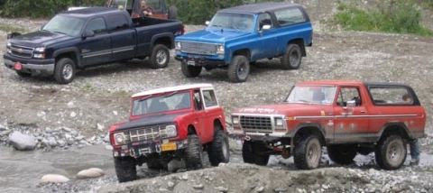 1978 Ford Bronco - A red 1978 Ford Bronco is parked on a rocky incline, with other off-road vehicles in the background.