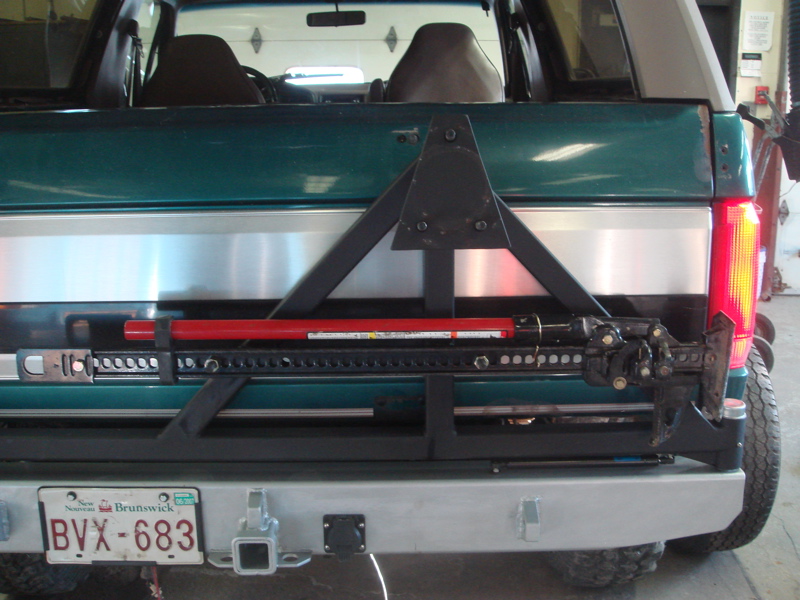 Green 1996 Ford Bronco rear bumper with a mounted spare tire carrier, jack, and red bar