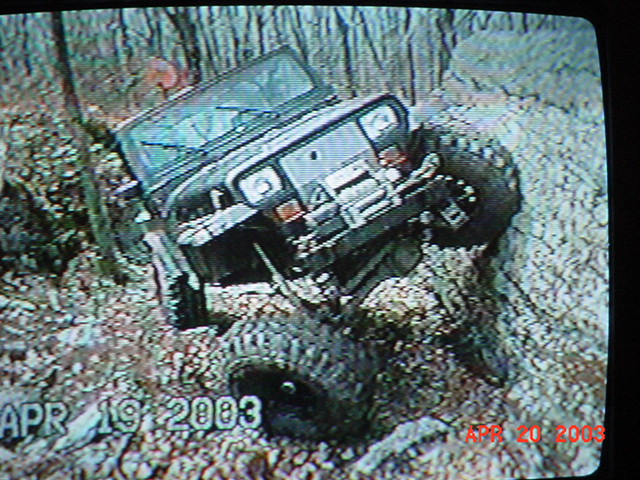 TV screen showing a lifted dark Jeep 4x4 climbing a rocky muddy off-road trail