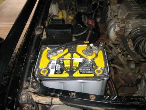 1986 Ford F-150 - Close-up of a car battery with visible text and wiring in the engine compartment.