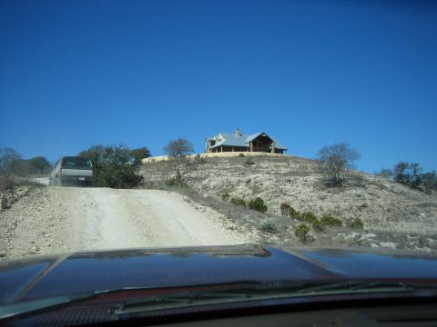 1996 Ford Bronco - A silver SUV ascends a dusty track on a clear day, with a large house visible on the hilltop.