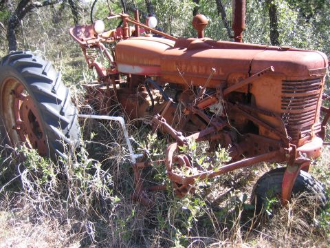 1996 Ford Bronco - An old, weathered tractor sits abandoned in a field, partially obscured by tall grass and brush.