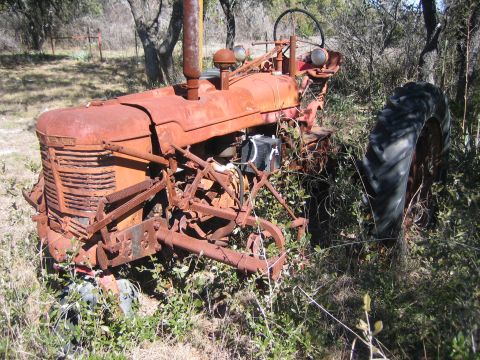 1996 Ford Bronco - An old, rusted tractor sits abandoned in overgrown brush, its large rear tire partially obscured by weeds.