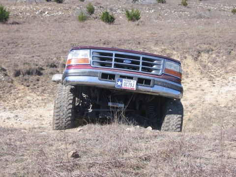 1996 Ford Bronco - A maroon Ford Bronco is shown tilted on a dry, grassy incline, with its front end angled towards the camera.