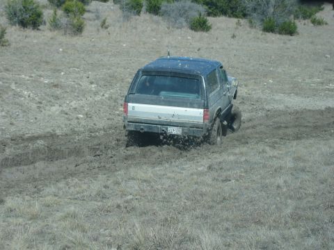 1996 Ford Bronco - A Ford Bronco navigates a muddy terrain, kicking up dirt as it goes.