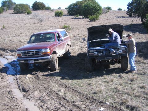 1996 Ford Bronco - Two trucks are stuck in the mud on a dry, grassy hillside with scattered trees.