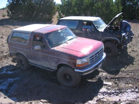 1996 Ford Bronco - Two Ford Broncos are stuck in the mud, one with its hood open while a person works on the engine.