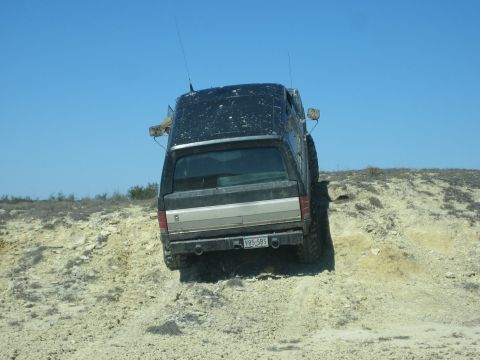 1996 Ford Bronco - A black SUV navigates a steep, rocky incline under a clear blue sky.