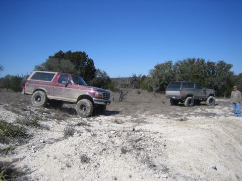 1996 Ford Bronco - Two Ford Broncos, one red and one gray, are parked on a dirt terrain under a clear blue sky.