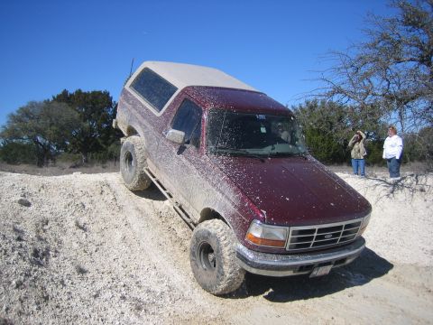 1996 Ford Bronco - Mud-covered 1996 Ford Bronco climbing a dirt hill off-road.