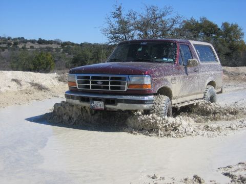 1996 Ford Bronco - This 1996 Ford Bronco is navigating a muddy off-road trail under a clear blue sky.