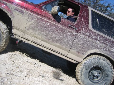 1996 Ford Bronco - A mud-covered 1996 Ford Bronco navigates a rough, off-road terrain.