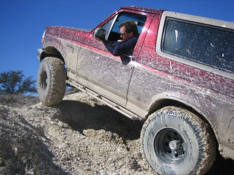 1996 Ford Bronco - Muddy 1996 Ford Bronco navigating a steep, rocky trail under a clear blue sky.