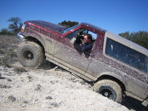 1996 Ford Bronco - A red SUV navigates a dirt path off-road, covered in mud.