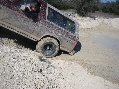 1996 Ford Bronco - A muddy 1996 Ford Bronco navigates a challenging off-road terrain with a driver visible inside.